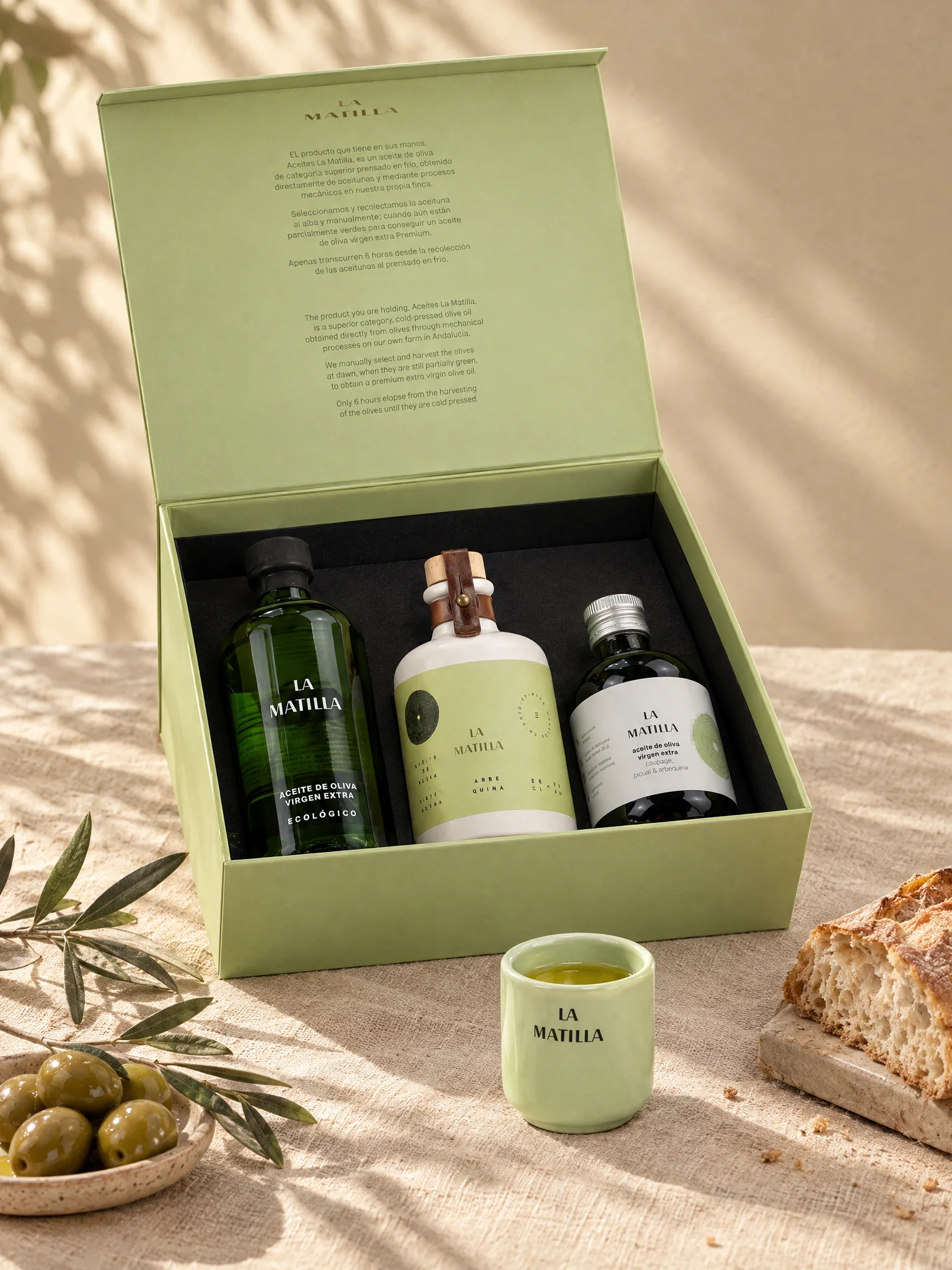 La caja de cata abierta en una mesa de lino, con el vaso catador servido, aceitunas y pan